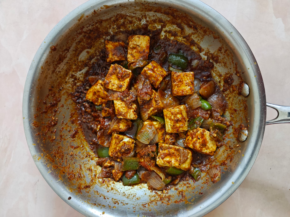 Kadai Paneer in a pan with paneer cubes, onions and green bell peppers coated in thick masala, ready to serve