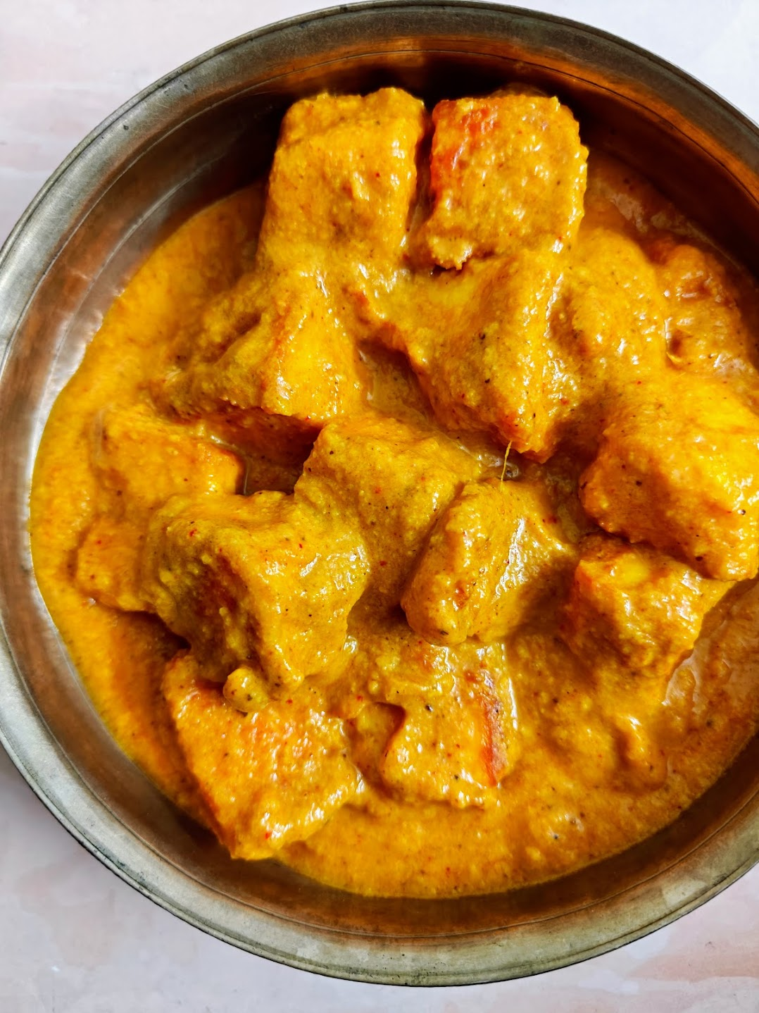 Bowl of paneer butter masala with golden paneer cubes in thick orange gravy.