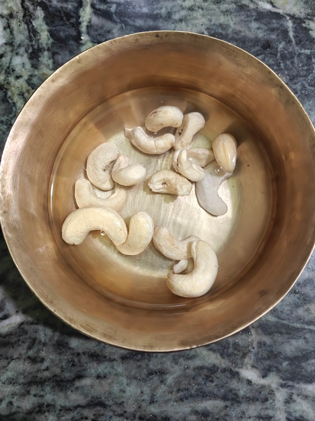 Cashews soaking in warm water in a small metal bowl.