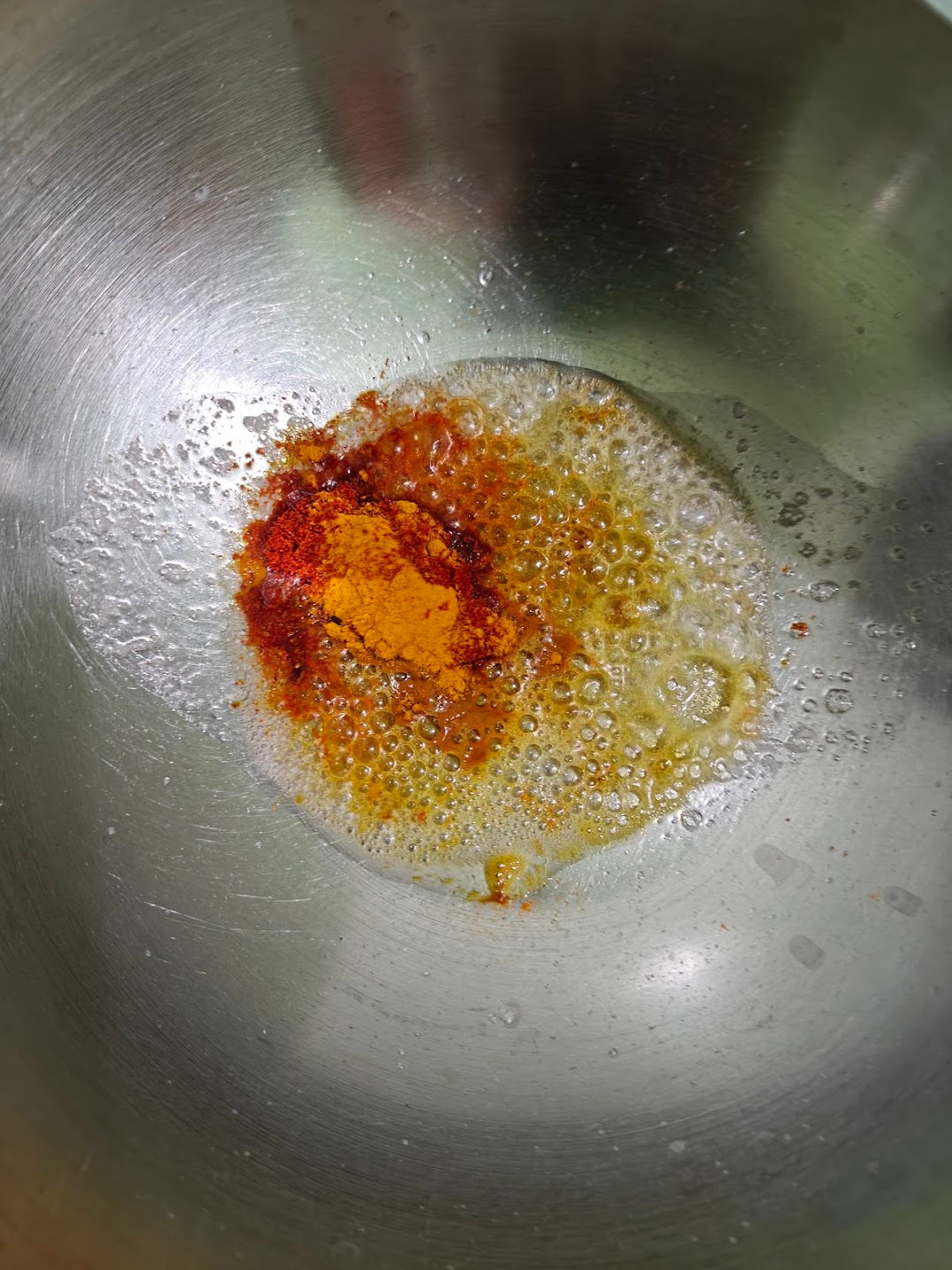 Turmeric and red chilli powder added to bubbling butter in a pan.