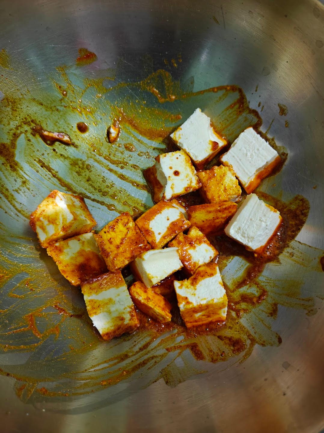 Paneer cubes being coated in spiced butter with turmeric and red chilli powder.