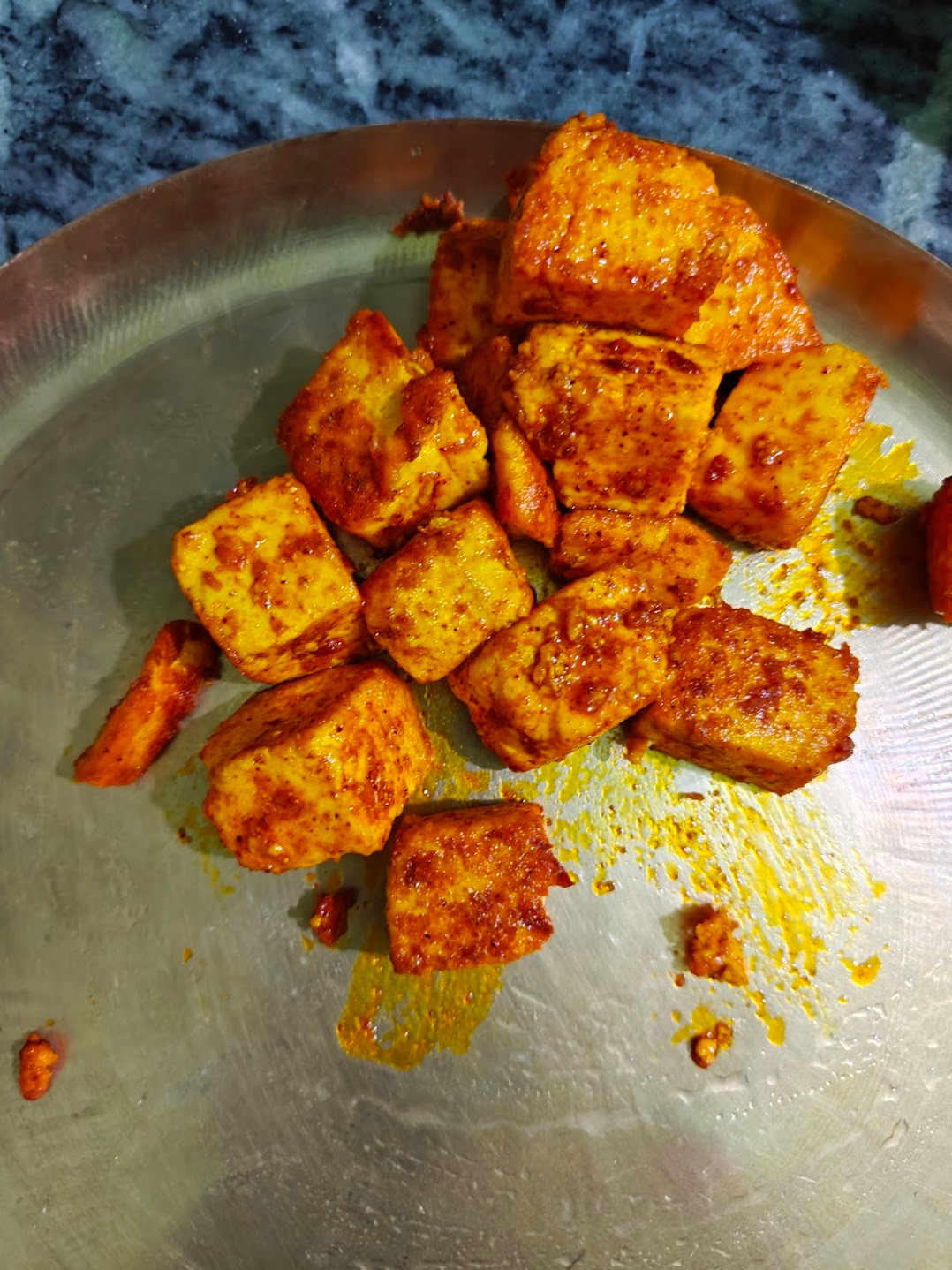 Lightly browned spiced paneer cubes set aside on a metal plate.