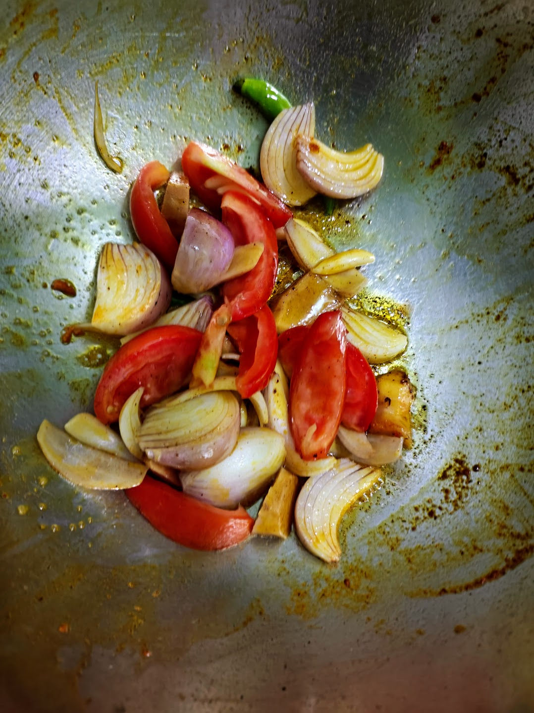 Chopped tomatoes, onion, ginger, garlic and green chilli cooking together in a pan.