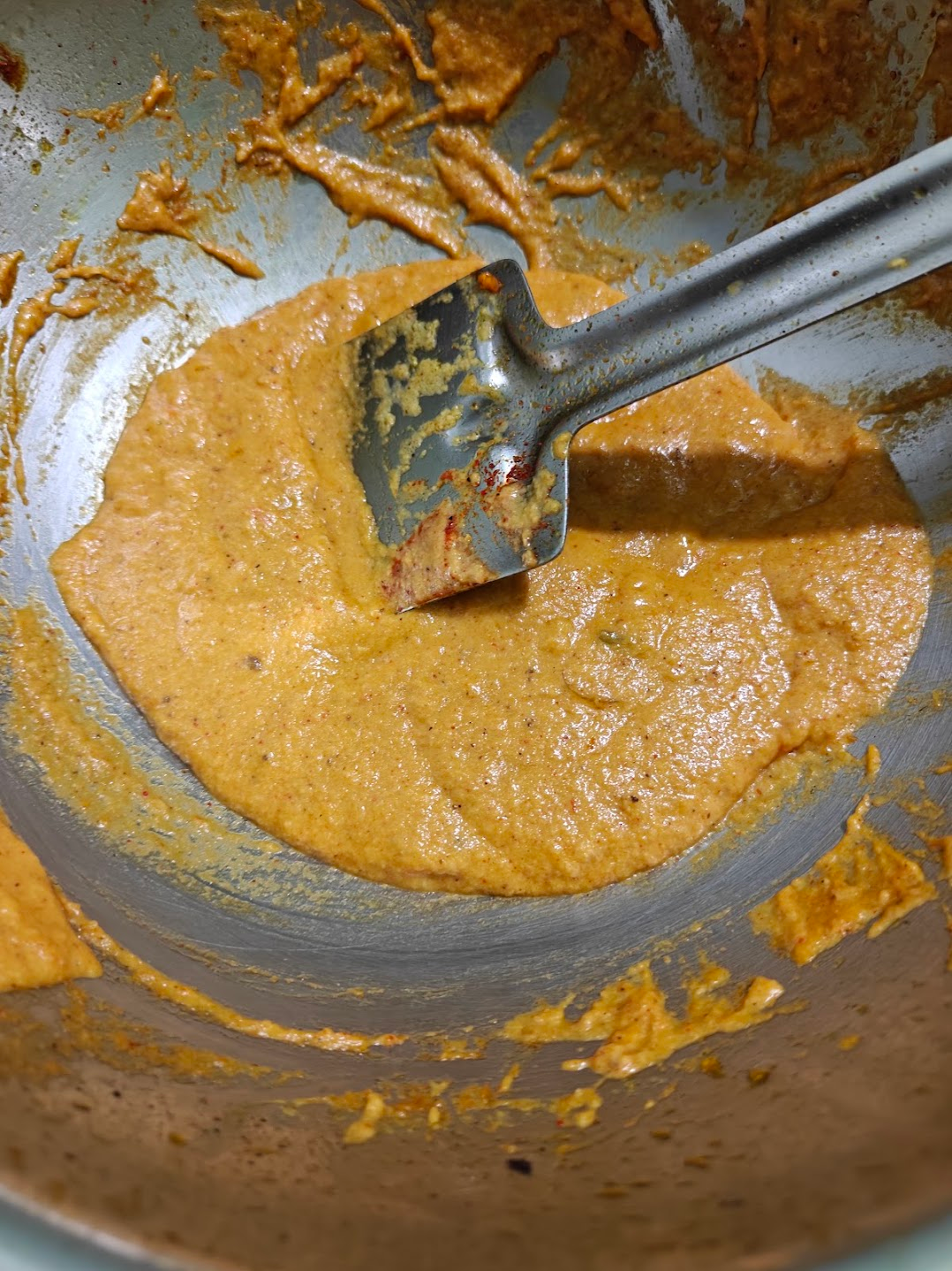 Smooth paneer butter masala gravy cooking in a pan with a metal spatula.