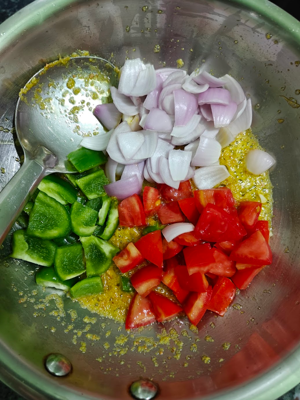 Onions, tomatoes and green bell peppers sautéing in the pan